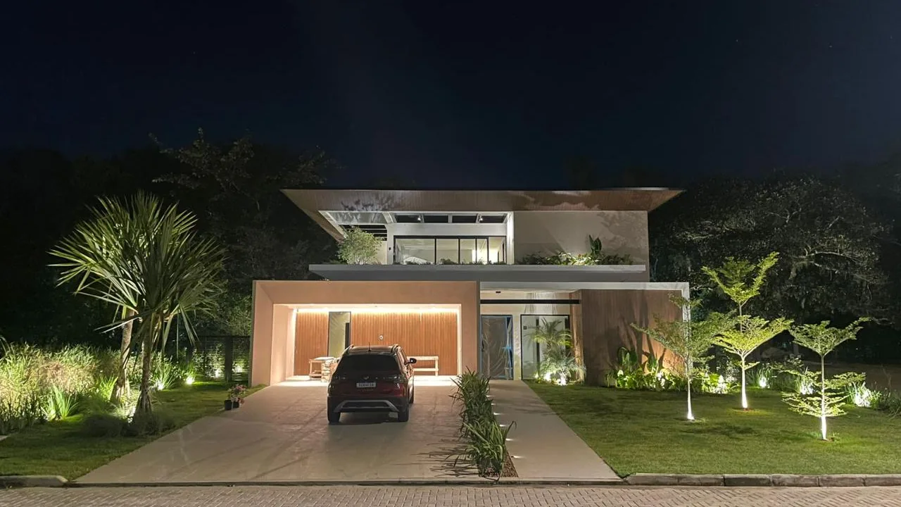 Fachada de casa à noite com o jardim iluminado